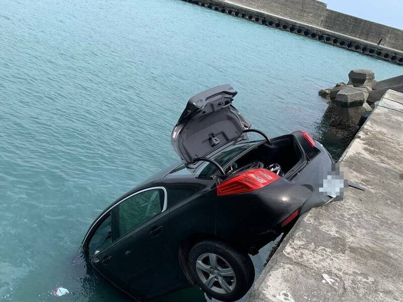 疑因未拉手煞車，停放在金樽港區堤岸的黑色轎車「倒頭栽」墜海。（記者陳賢義翻攝）
