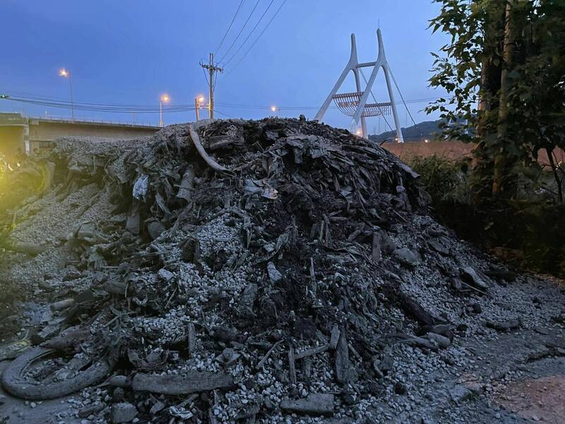 苗栗縣銅鑼鄉客屬大橋下防汛道路一帶，昨（21）日晚間又遭棄置大量疑似工地廢棄物，且在道路上「倒好倒滿」，害居民返家通行受阻。（徐裕逢提供）