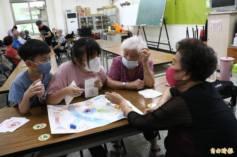 高子崴（左2）和黃梓宸（左1）是表姊弟，兩人與長者一起玩自製的「湯仔城地圖桌遊」。右黑衣者為王吳月美阿嬤。（記者蔡昀容攝）