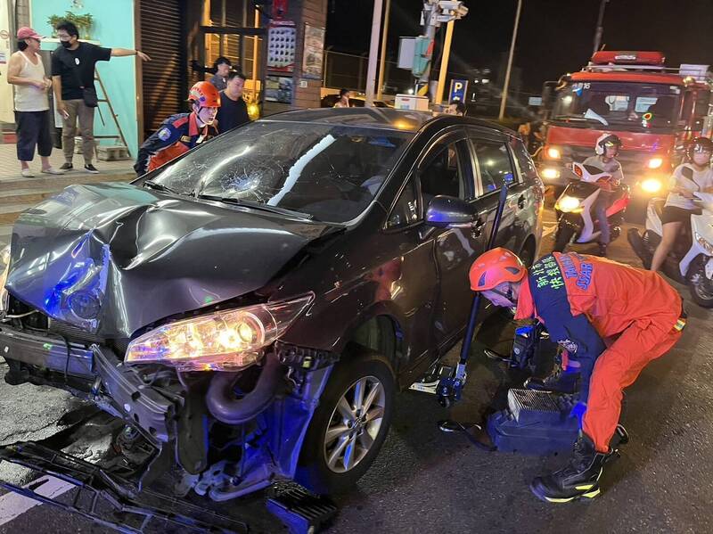 新北市淡水鬧區今晚發生汽車連撞11輛機車連環車禍，1名騎士連人帶車捲入車底遭拖行，消防人員以救助器材頂起車身救出。（記者吳仁捷翻攝）