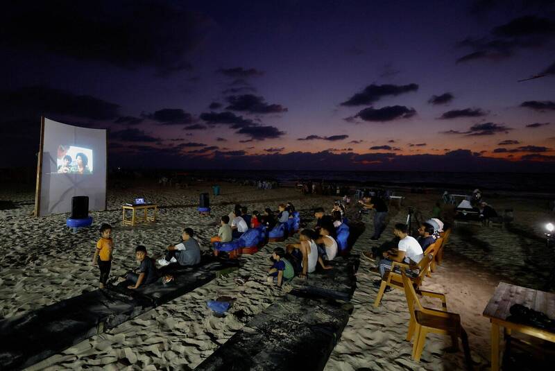2023年8月11日，巴勒斯坦民众在加萨市滨海沙滩上举行的露天电影院活动中，聚精会神地观看由投影机放映的电影。（路透）(photo:LTN)