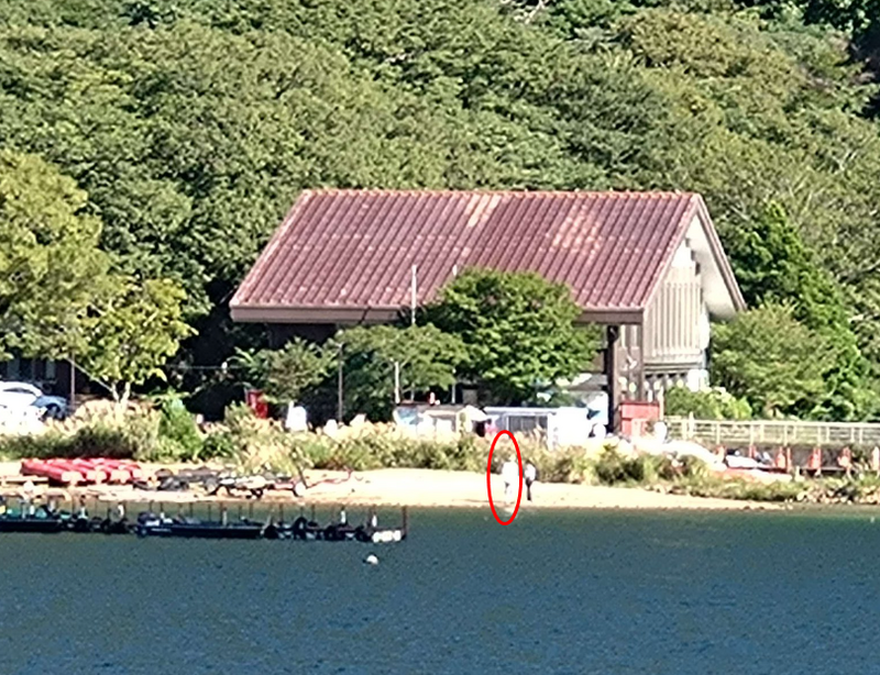 日本一名網友近日出遊，在湖邊拍獨照，身旁竟出現詭異人影（紅圈處）。（圖翻攝自推特@Bibliophile_ykr）