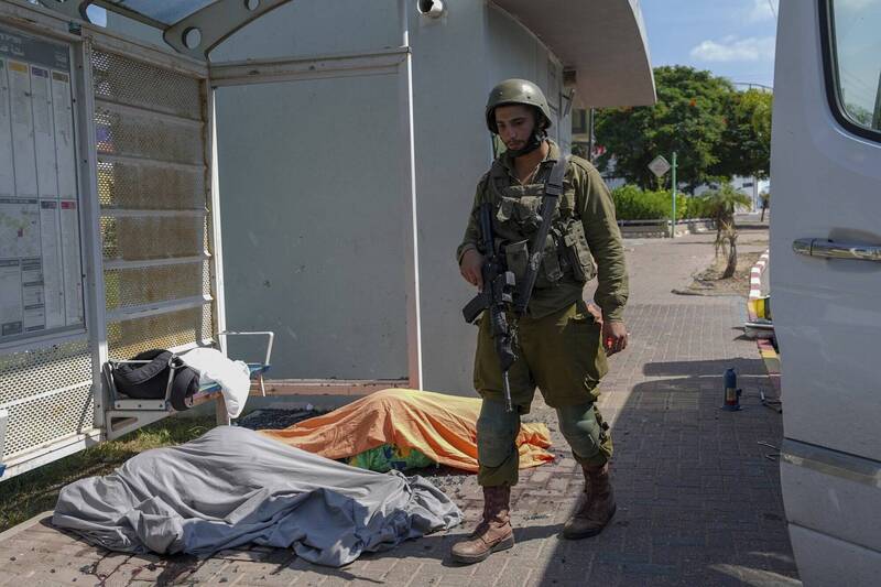 以色列驻美大使馆表示，以国目前共有300人死亡、1800人受伤、100人被俘。图为以军士兵在遭射杀的平民遗体旁站岗。（美联社）(photo:LTN)