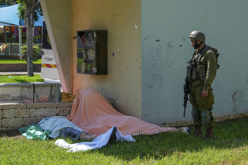 以色列边境城市斯德罗特，一名以军士兵站在以色列平民的尸体旁。（美联社）(photo:LTN)