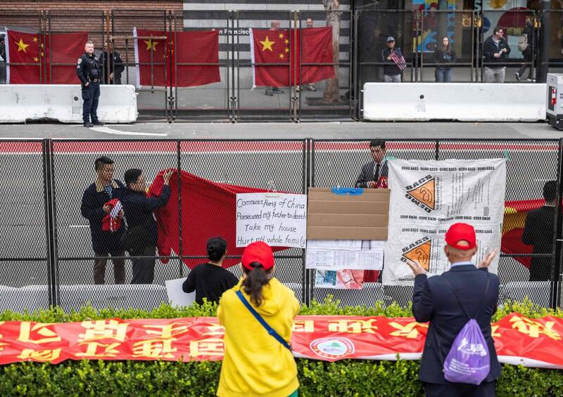 习近平到旧金山参加APEC峰会，不少中方人士提前到沿路准备欢迎，抗议人士更早一步在路边的铁丝网挂上抗议海报、标语，疑似中国官员拿五星旗和欢迎布条技巧地遮盖。（法新社）(photo:LTN)