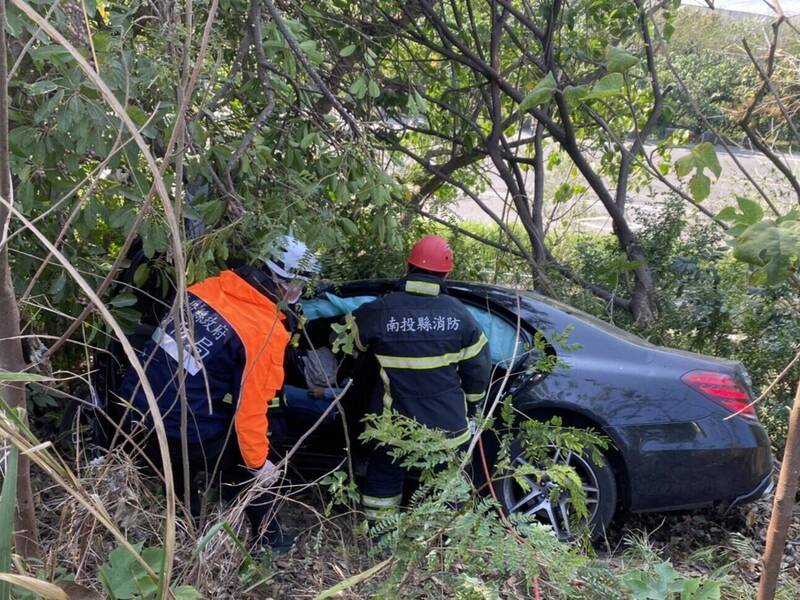 國道3號南下255K處，一輛黑色賓士S350轎車失控衝破護欄，最後墜落邊坡卡在草叢，車上氣囊全爆，消防人員趕赴救援。（南投縣消防局提供）