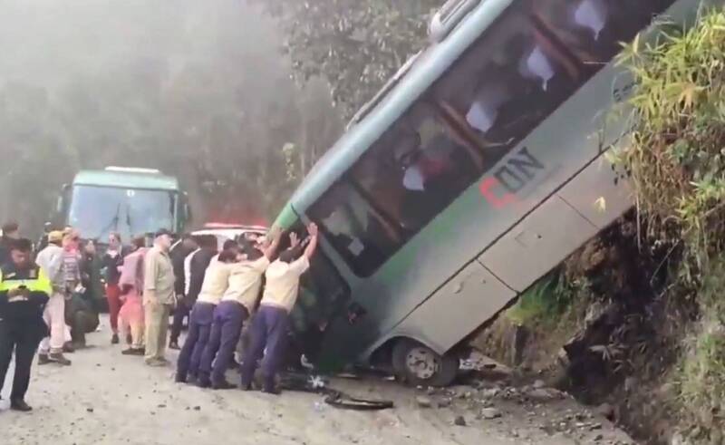 失事遊覽車車頭撞到路面，車身傾斜在斜坡上，許多民眾合力支撐着車身以防再次翻覆。（圖擷自X）