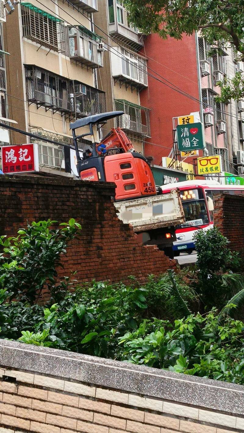 張姓男子載運挖土機經過淡水鬧區，倒車時疑剎車故障，撞破百年真理大學圍牆，警方到場幸無人受傷，肇因及責任歸屬，仍待調查釐清。（記者吳仁捷翻攝）