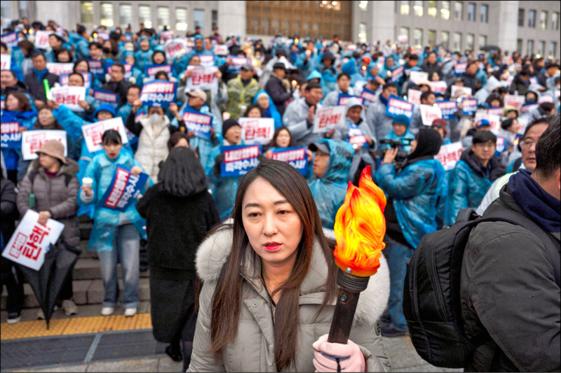 五日在首爾，一名婦女手持塑膠火炬，加入抗議南韓總統尹錫悅的燭光守夜活動。（美聯社）