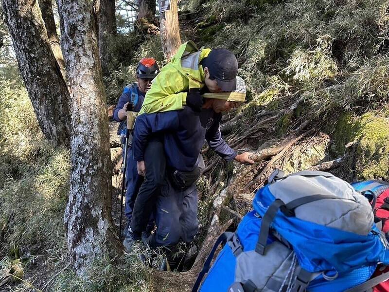 山友（綠衣）獨攀單攻八通關山不慎摔到頭破骨折，搜救人員以背負方式將人移至直升機起降點吊掛。（圖由南投縣消防局提供）