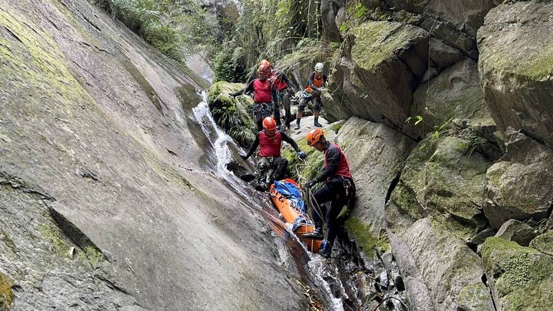 新竹縣消防局山搜人員冒險在山谷中，要把張姓男子的遺體搬運上至少80公尺高的峭壁。（竹縣府消防局提供）