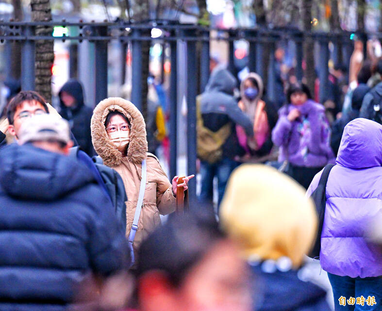 People in winter clothing walk on a street in Taipei yesterday.
Photo: Fang Pin-chao, Taipei Times