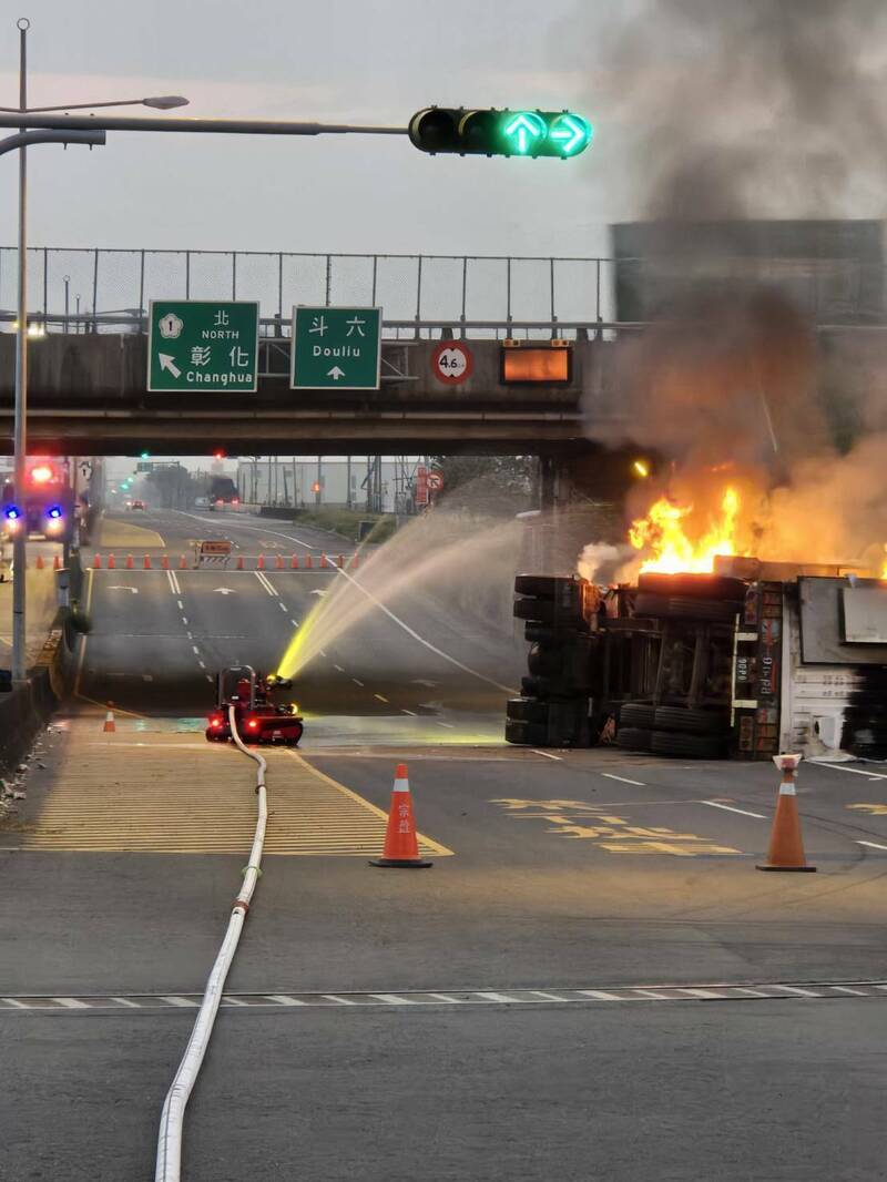 一輛載運太陽能儲能櫃的貨車昨天翻覆在國1虎尾交流道下方聯絡道路上，車上儲能櫃今早起火燃燒，雲林縣消防局以機器人用水柱防護車頭避免火勢擴大。（雲林縣消防局提供）