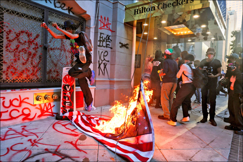 美國總統川普下令聯邦移民官員鎖定民主黨執政的大城市，擴大驅逐無證移民。圖為抗議者在洛杉磯切克斯希爾頓酒店前焚燒美國國旗。（路透）