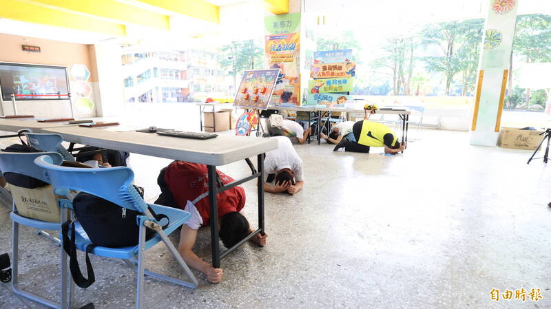 新北市教育局今於頂埔國小舉辦複合型防災演練，地震警報響起時，現場人員趴在桌下掩護。（記者黃政嘉攝）