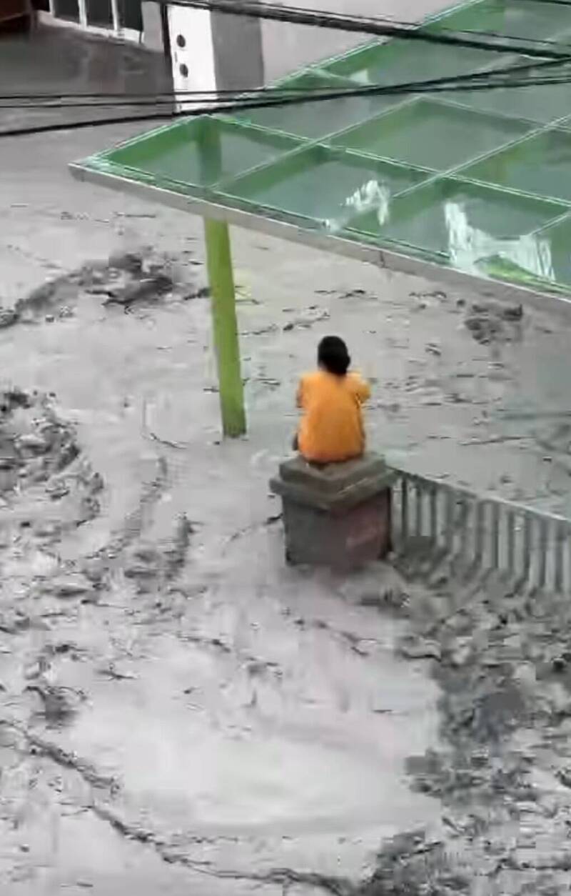 一名女子獨自坐在自家外牆上，無助地看著自己的家園被大水肆虐。（圖翻攝自楊華美臉書）