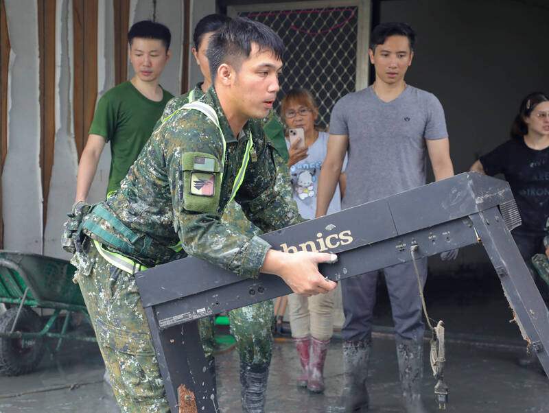 被大水沖壞掉的電子琴架子，官兵一個人挺腰搬出，屋主在旁確定已損壞才搬運。（花東防衛指揮部提供）