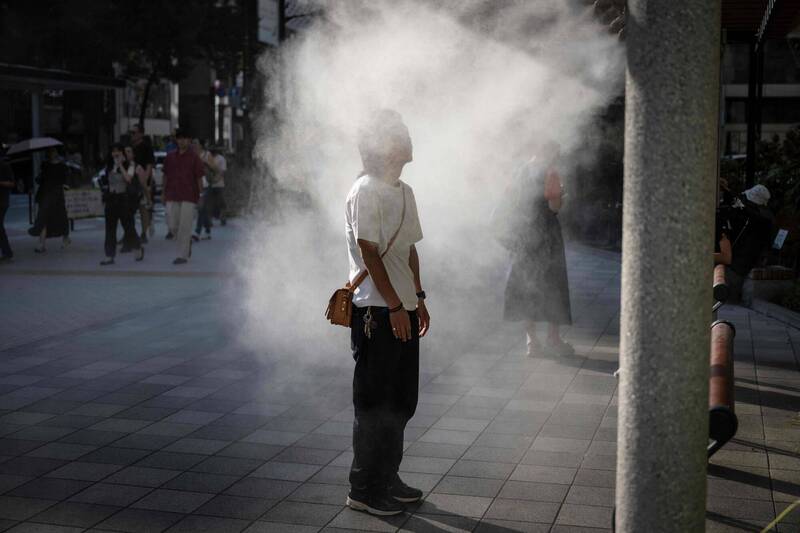 9月間在炎熱的東京街頭，一名男子站在水霧系統下降溫。（法新社）