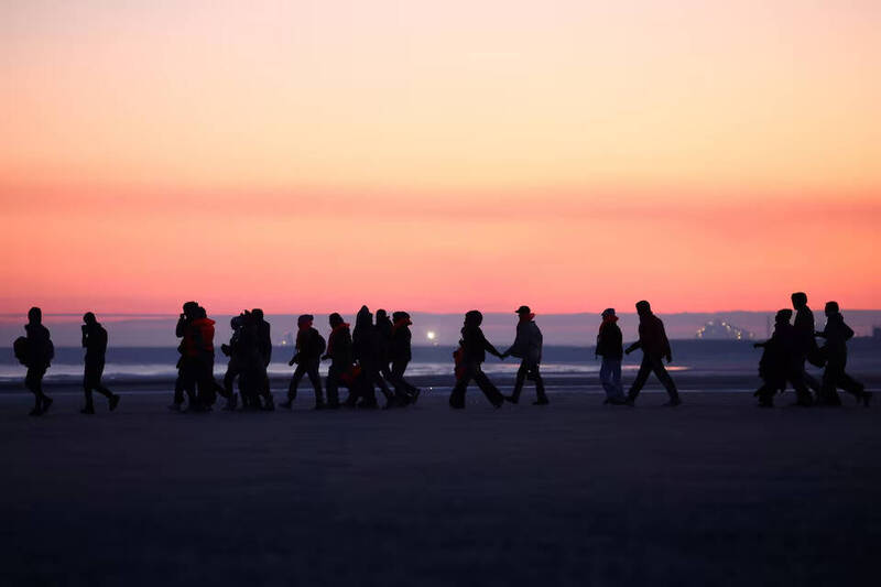 移民在黎明时分徒步走过法国北部海滩，准备搭乘小船冒险穿越英吉利海峡前往英国。正是这不断涌入的「小船移民潮」，促使英国政府拟推动史上最严苛的庇护政策改革。（路透资料照）