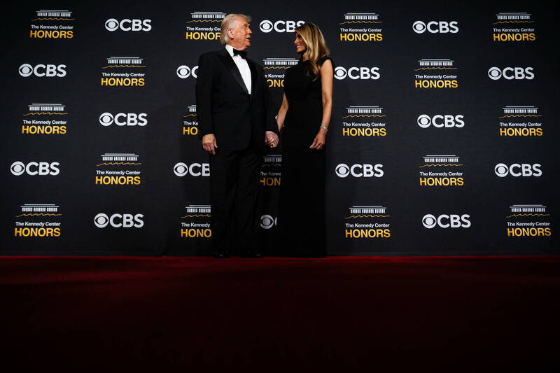 2025年12月7日，美国总统川普与第一夫人梅兰妮亚在「甘迺迪中心荣誉奖」颁奖典礼的红毯拍照背板前留影。背板上清楚可见尚未更名的「甘迺迪中心」与转播单位CBS的标志与字样。（美联社）