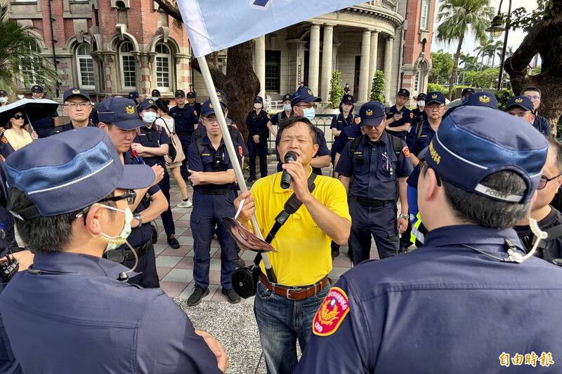 台灣國理事長陳峻涵25日站在行政院對面的街口，面對重重警力包圍，高舉標語旗幟隔空回嗆民眾黨。（記者陳治程攝）