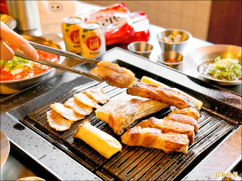 金豬食堂採用韓國鑄鐵烤盤，導熱與保溫效果極佳。每桌有專人在桌邊代烤，醬菜、生菜與醬料皆可續。（記者郭宣暄攝）