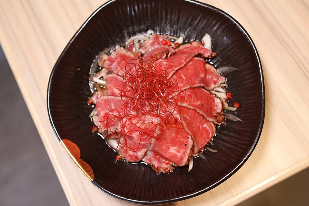 「生牛肉」售價390元，選用美國牛小排輕微炙燒表面後切片，搭配水果醋、紅椒粒與辣椒絲，整體風味清爽。（圖／記者郭宣暄攝）