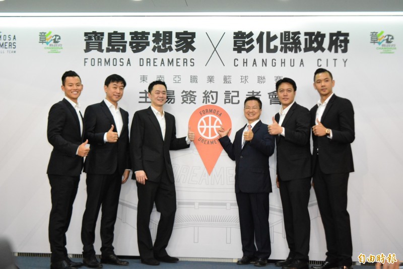 球隊成員和彰化縣長魏明谷，站在大型布幕看板前，排成勝利「V」的圖案。（記者張聰秋攝）