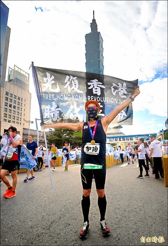 來自香港的跑者,身穿黑色跑衣,並舉著「光復香港,時代革命」的旗幟邁入終點,期盼藉由台北馬,向國際社會傳遞「護民主,挺自由」的訴求。(記者方賓照攝) 來自香港的跑者,身穿黑色跑衣,並舉著「光復香港,時代革命」的旗幟邁入終點,期盼藉由台北馬,向國際社會傳遞「護民主,挺自由」的訴求。(記者方賓照攝)