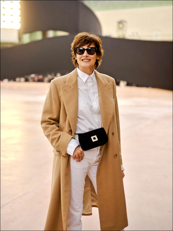 Ines de la Fressange一身白色褲裝造型搭配卡其色大衣，斜背CHANEL黑色掀蓋包打造看秀造型。