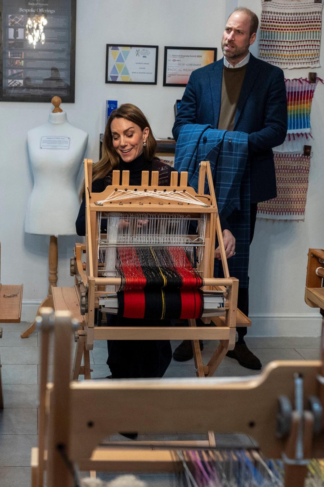 凱特王妃試用織布機，威廉王子拿著老婆的外套耐心等待。(美聯社)