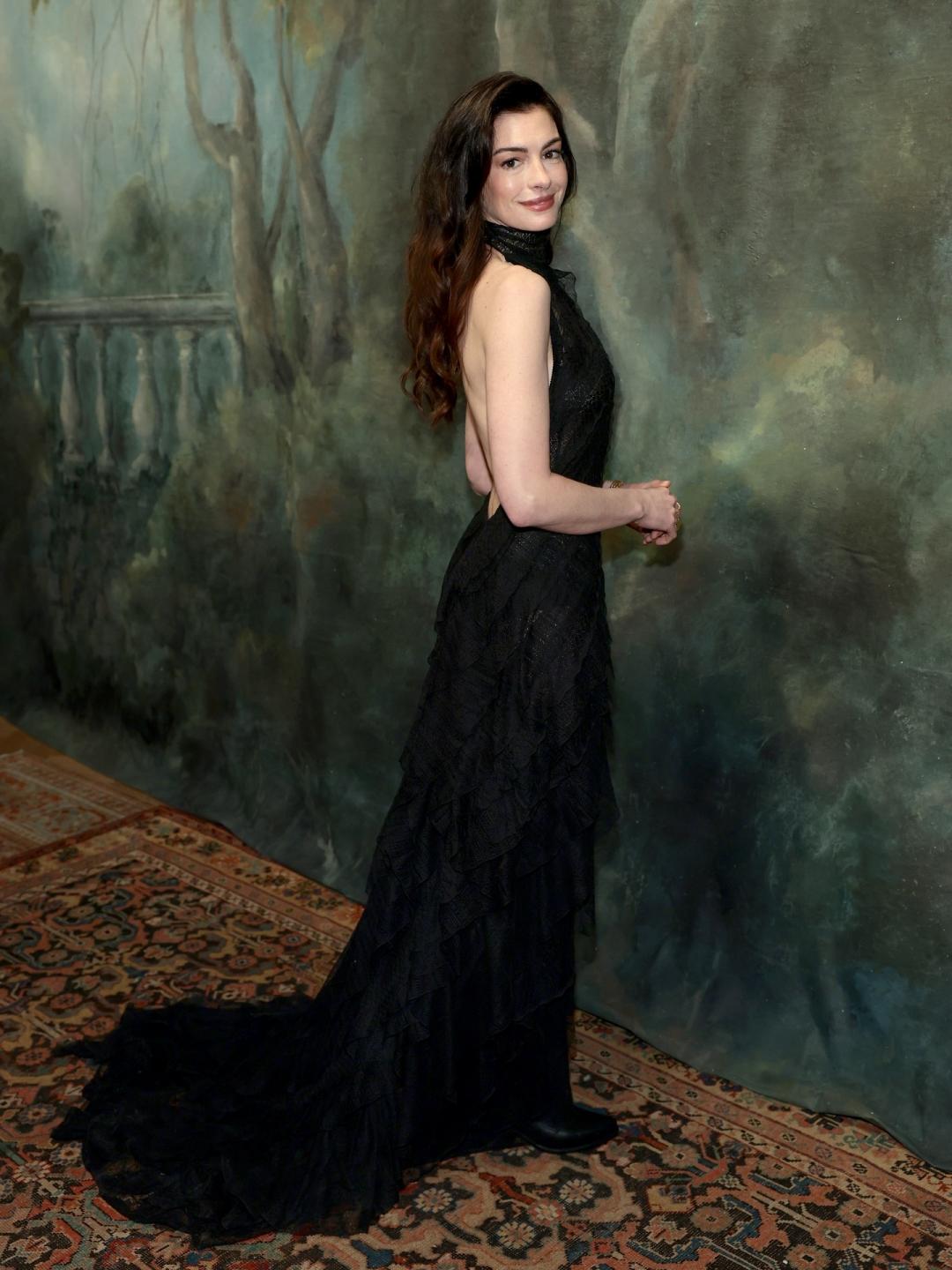 安海瑟薇穿著一襲全黑削肩露背高領禮服，斜向織紋設計透過異材質的拼接營造出豐富的視覺層次感，延伸至地面的魚尾長裙襬，展現出流動感曲線美。