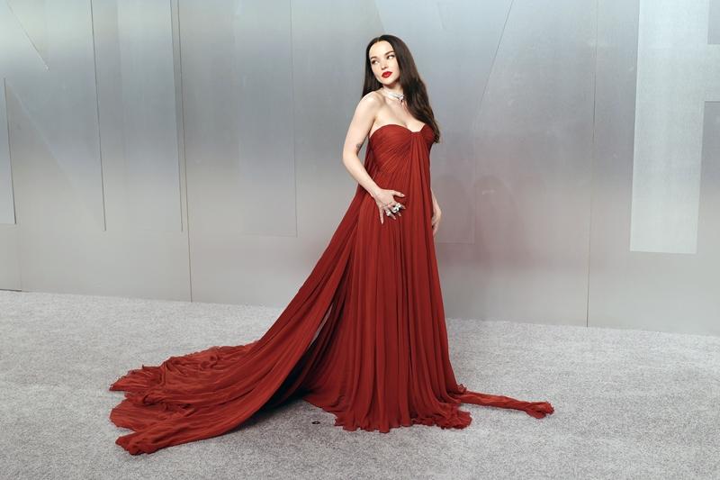 Dove Cameron身穿 紅色拖尾禮服 登場，垂墜布料營造戲劇感；搭配鑽石珠寶。