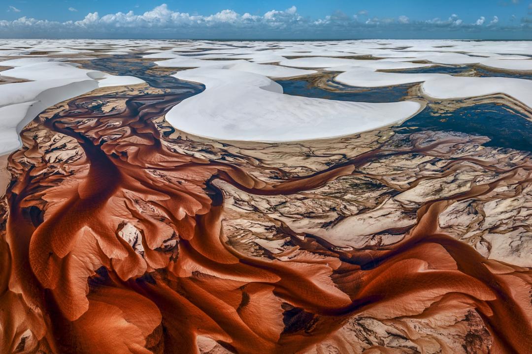 一條天然呈茶褐色的河流蜿蜒流經巴西千湖沙漠國家公園（Lençóis Maranhenses National Park）的白沙丘。