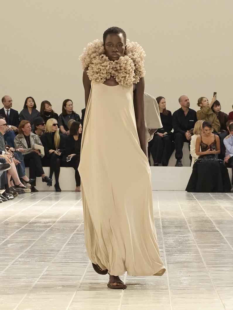 BALENCIAGA奶茶色長洋裝在頸間加入層層堆疊的立體裝飾，簡潔裙身與繁複頸飾形成對比。