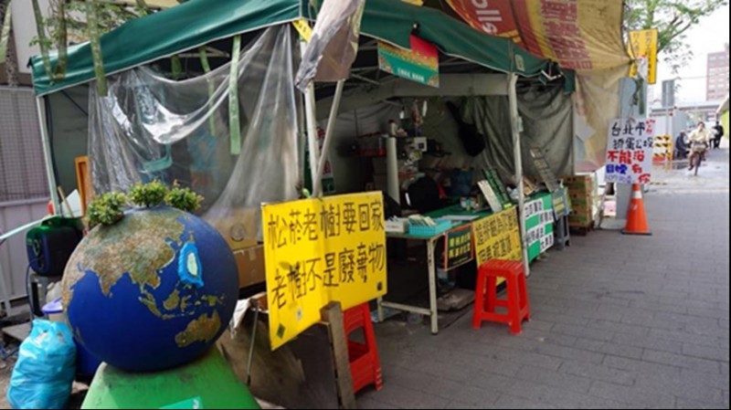 松菸志工團帳篷外寫著護樹拆巨蛋的標語。（攝／邱逸鈴）